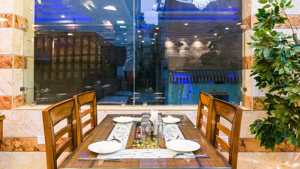 A dining area with a glass partition, wooden chairs, a marble-tiled table, and a chandelier.