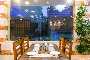 Un comedor con separador de vidrio, sillas de madera, mesa con mosaicos de mármol y un candelabro.