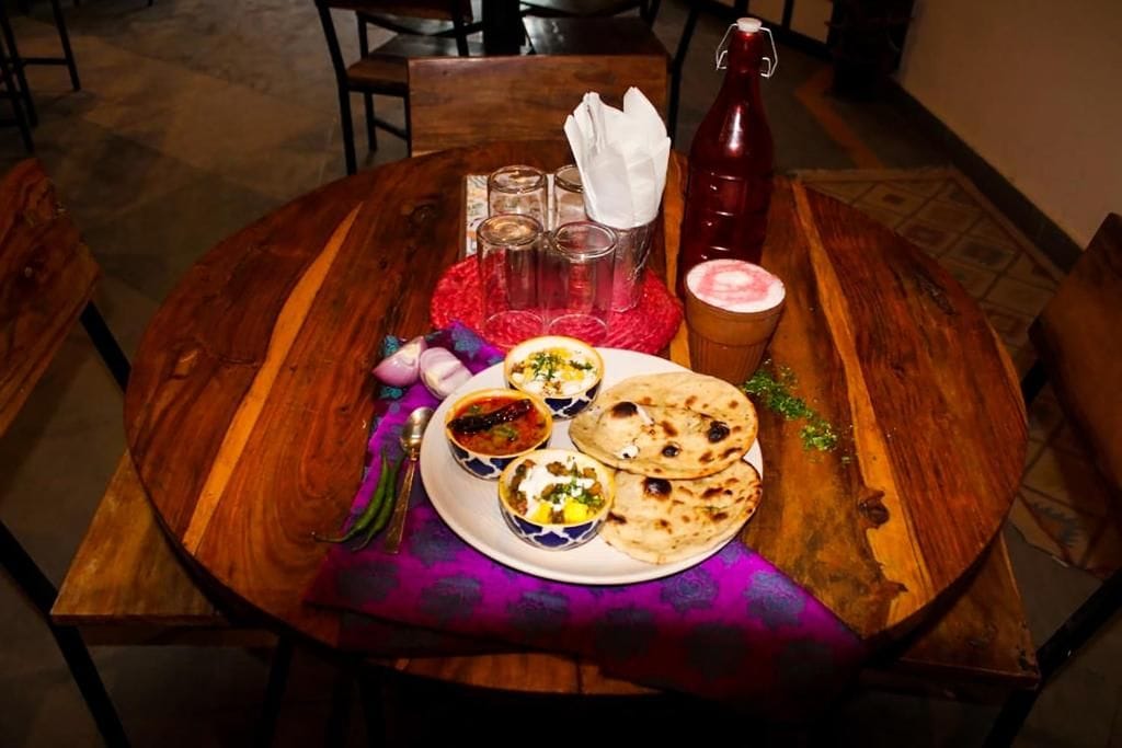 A round wooden table with a plate of food, including flatbreads and bowls of curry, a red bottle, and a glass of beverage.