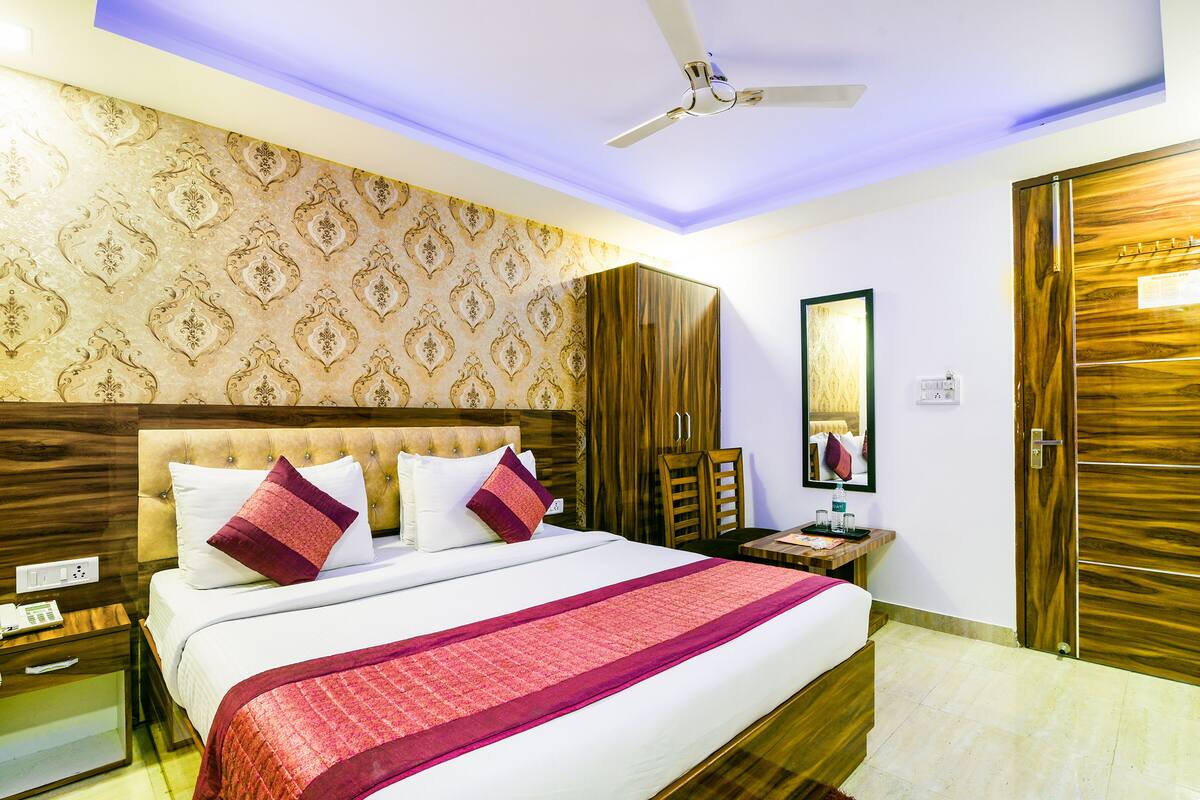 A hotel room with a large bed, a ceiling fan, a wardrobe, a bedside table, and a mirror.