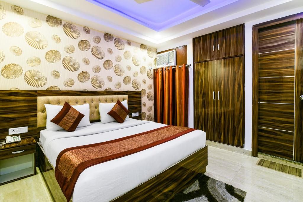 A hotel room with a large bed, wooden wardrobe, and a patterned wall.