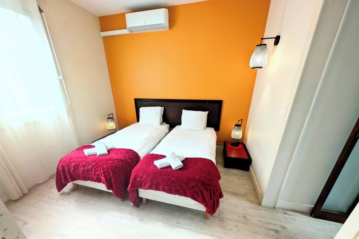A hotel room with two beds, a red blanket on each, a white ceiling, and a wall-mounted air conditioner.