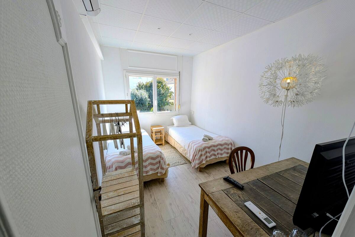 A bedroom with two single beds, a wooden ladder, a desk with a computer, and a decorative lamp.