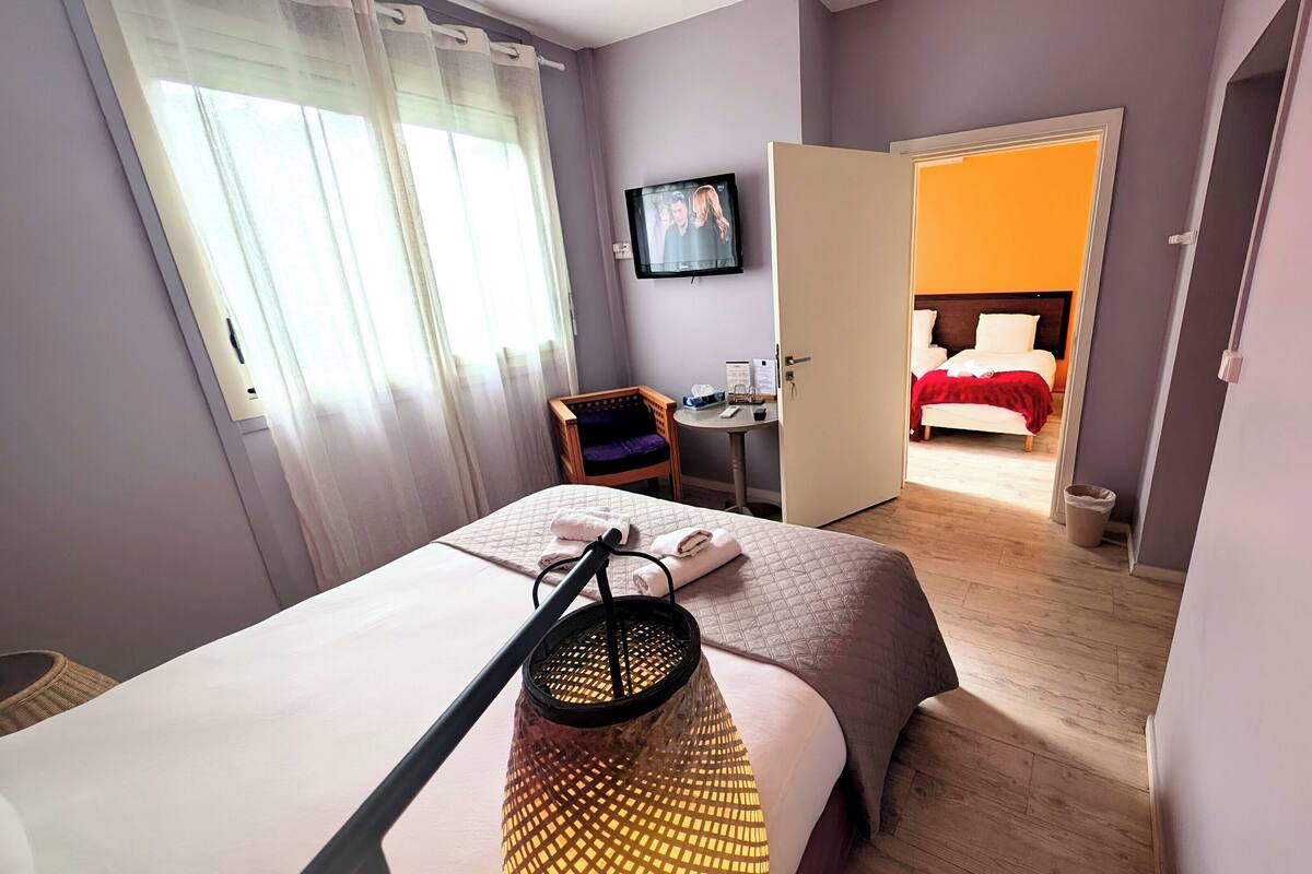 A hotel room with a bed, a desk, a chair, a TV, and a bathroom visible through an open door.