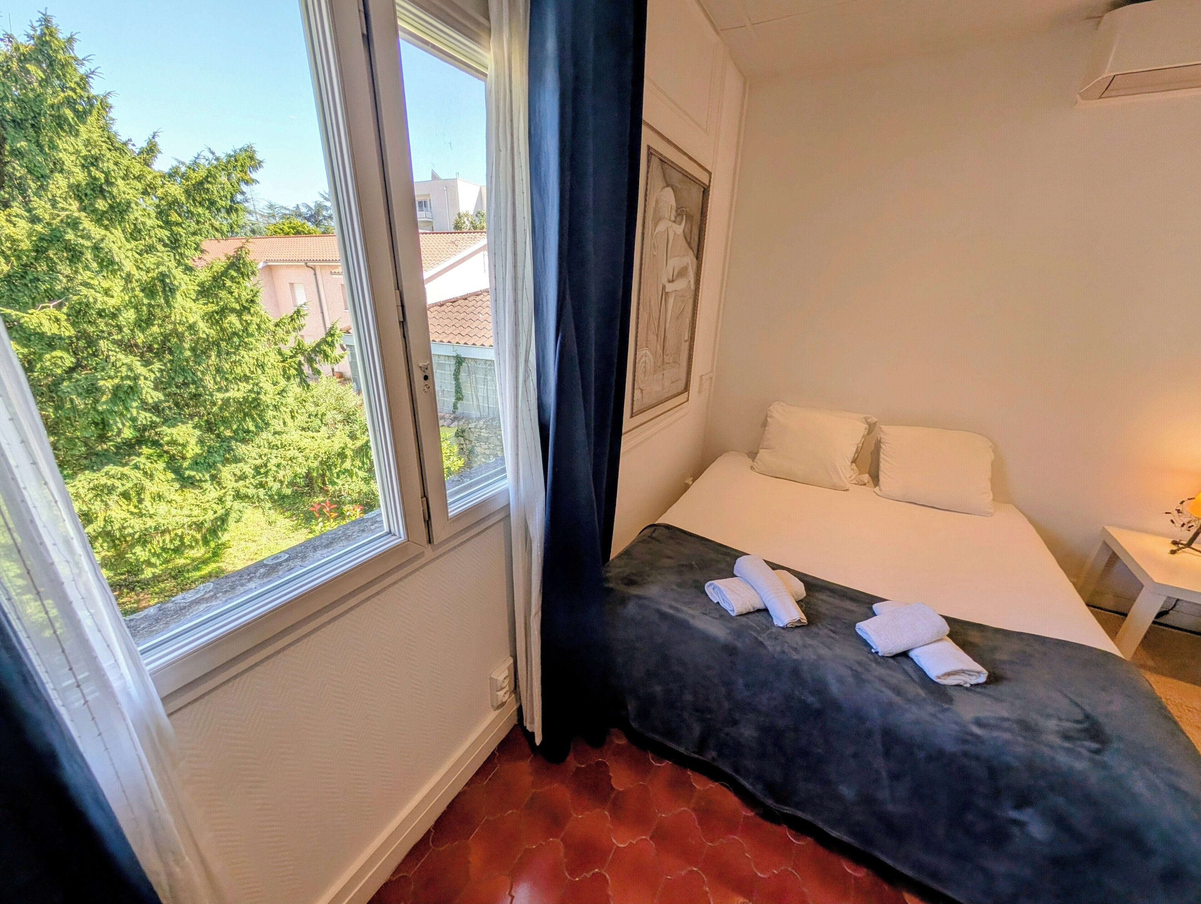 Quarto com cama, janela e vista para o verde lá fora.