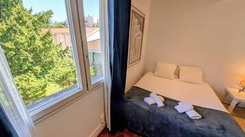 Quarto com cama, janela e vista para o verde lá fora.