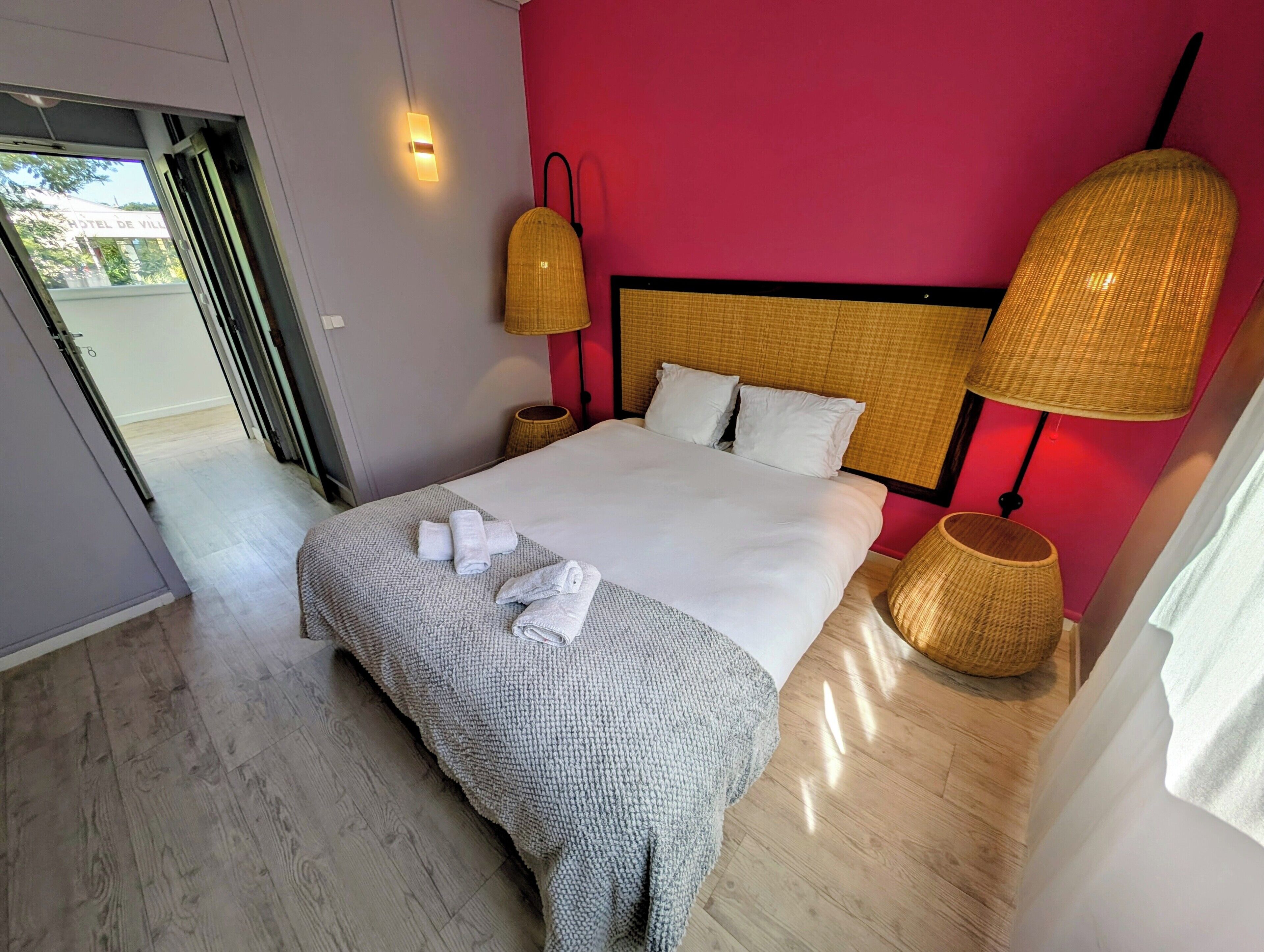 A neatly made bed with white linens and a grey blanket, two bedside lamps, and a door leading to an outdoor area.