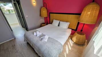 A neatly made bed with white linens and a grey blanket, two bedside lamps, and a door leading to an outdoor area.