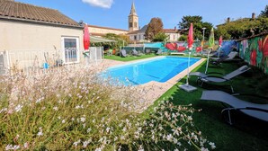 Ein Swimmingpool mit Liegestühlen und Sonnenschirmen, umgeben von einem Garten mit Blumen und einer Wand mit Wandgemälden.