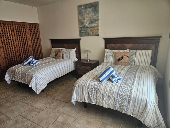 Two double beds with striped bedding, a wooden headboard, a nightstand with a lamp, and a wall-mounted painting.