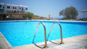 Une piscine dotée de rampes en métal, d’une eau d’un bleu limpide et offrant une vue sur un bâtiment et des arbres en arrière-plan.