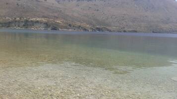 Un lago transparente con piedras visibles en la orilla y un paisaje montañoso al fondo.