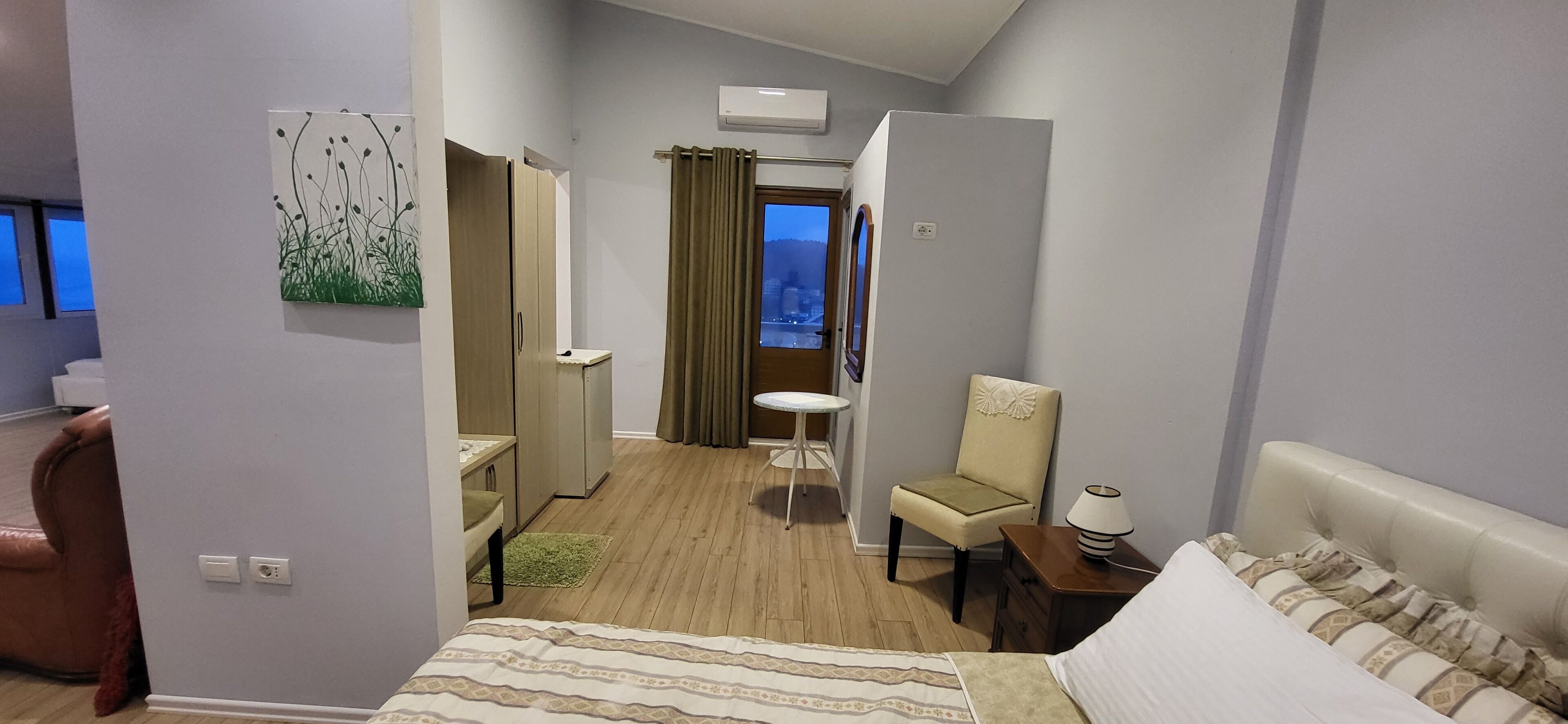 A hotel room with a bed, a chair, a desk, a small table, and a window with curtains.