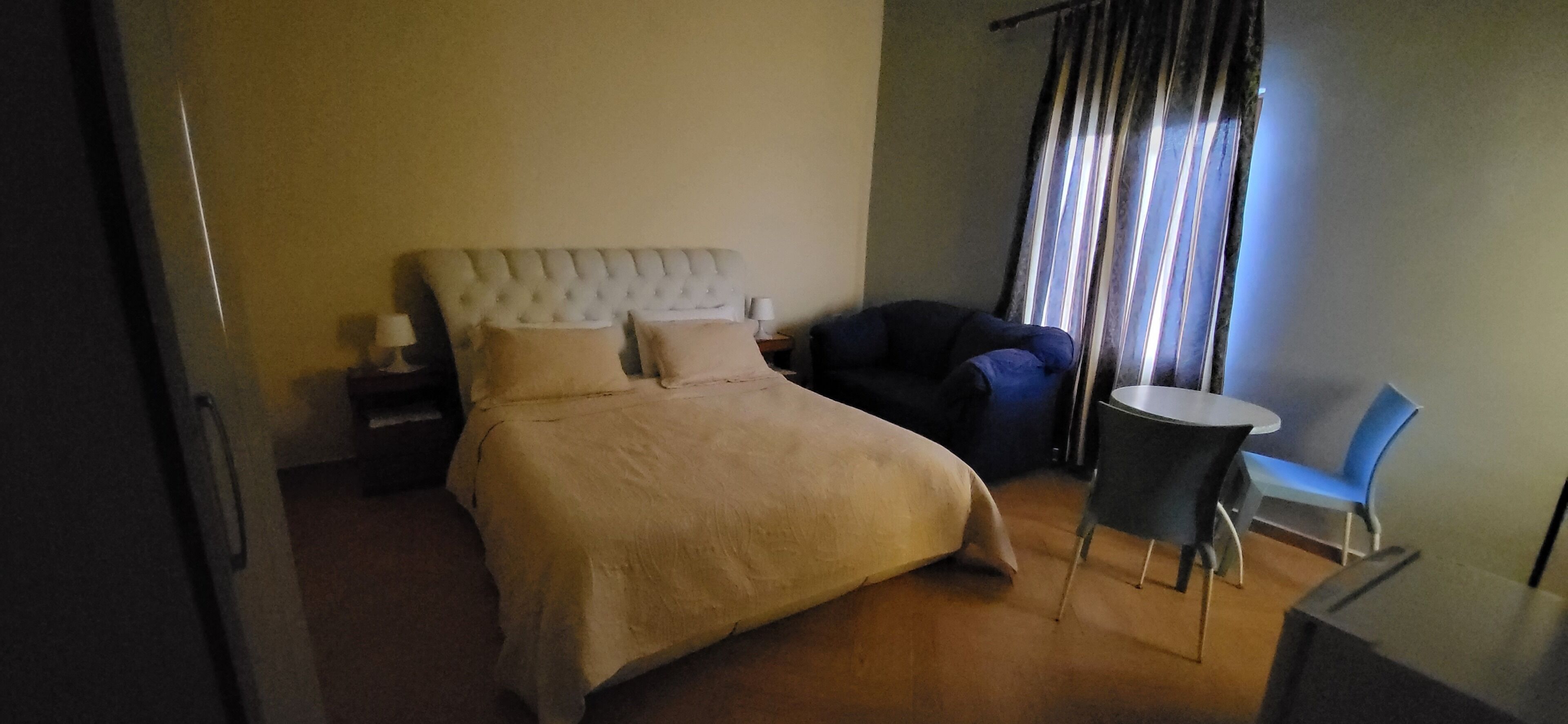 A bedroom with a bed, a chair, a small table, and a nightstand.