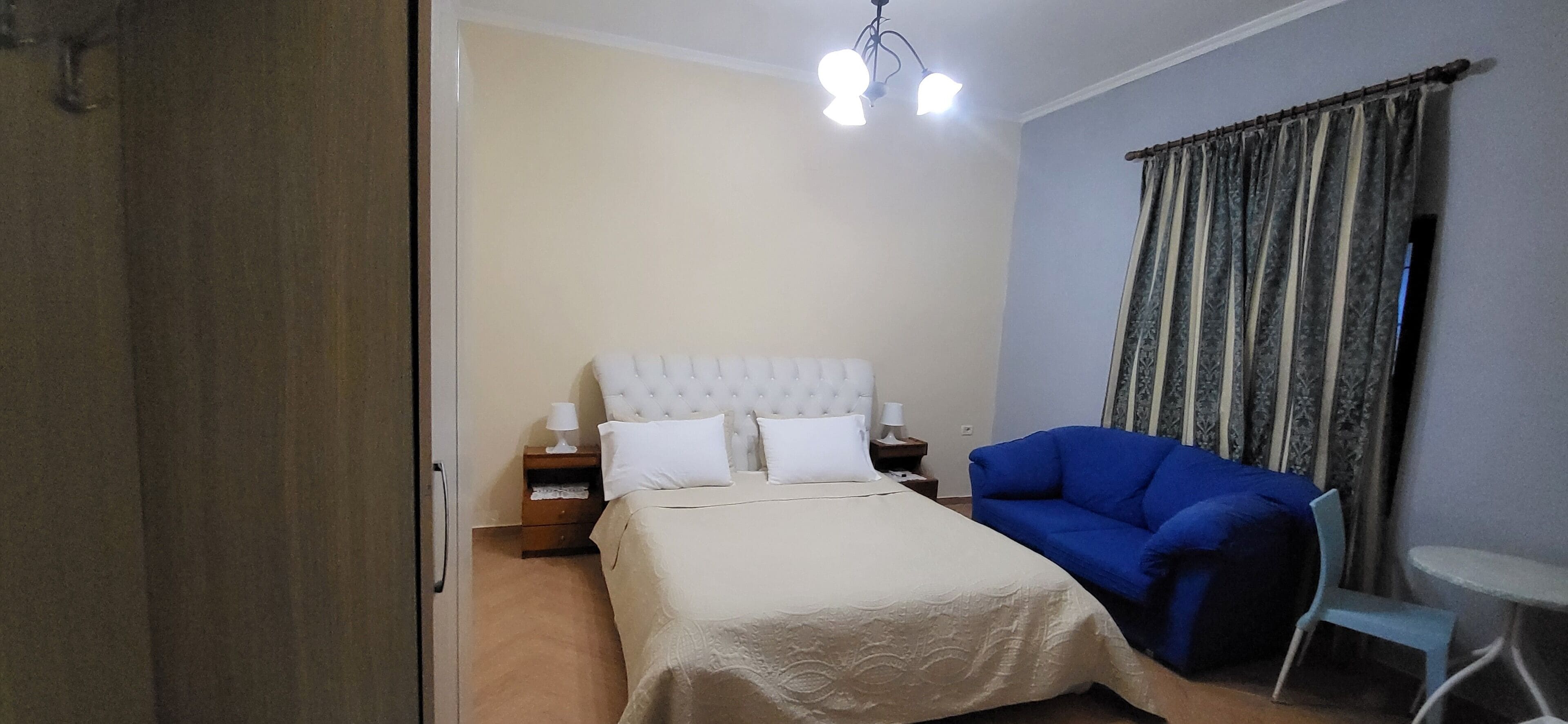 Ein Schlafzimmer mit einem Bett, einem blauen Sessel, einem kleinen Tisch und einem Nachttisch mit Lampen.