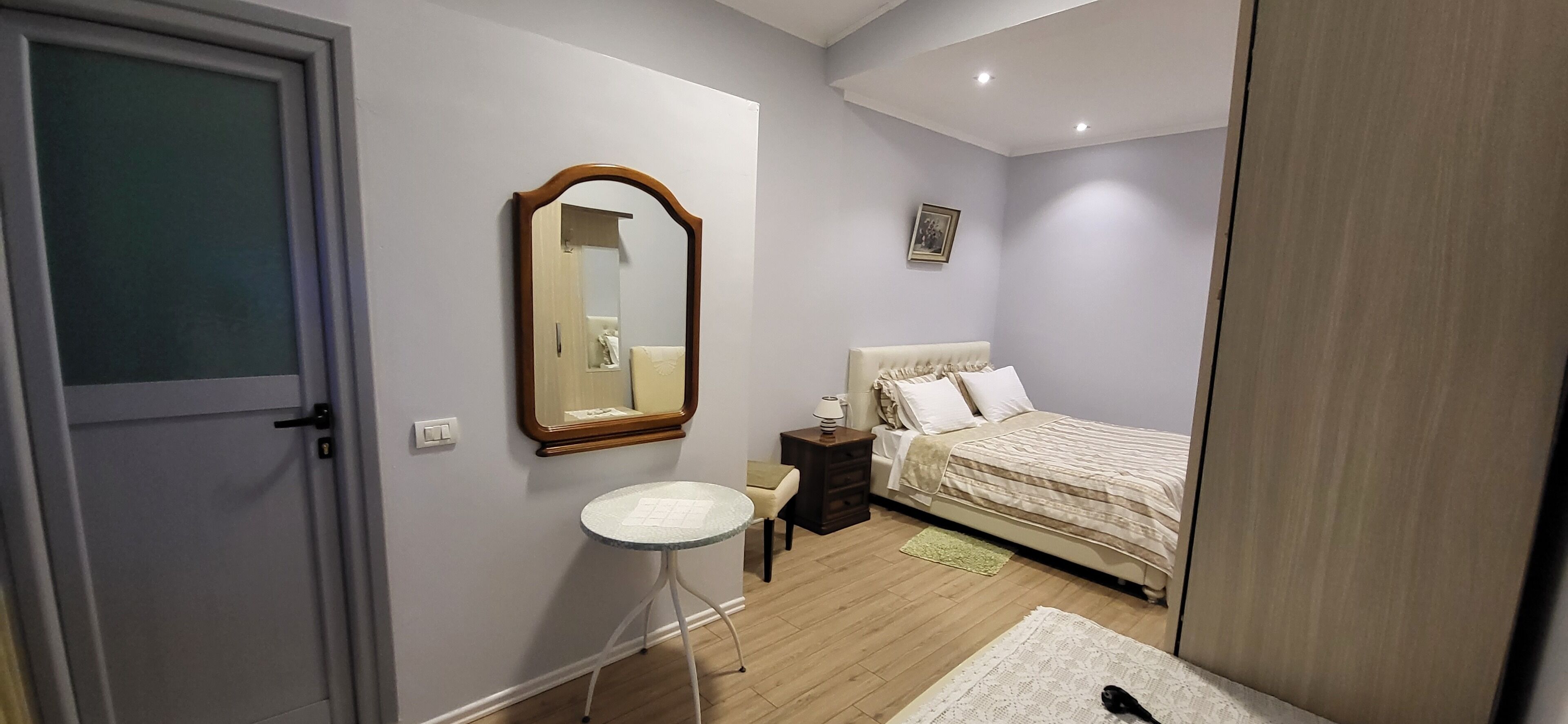 Un dormitorio con una cama, una mesita de noche, una silla, un espejo y una puerta.