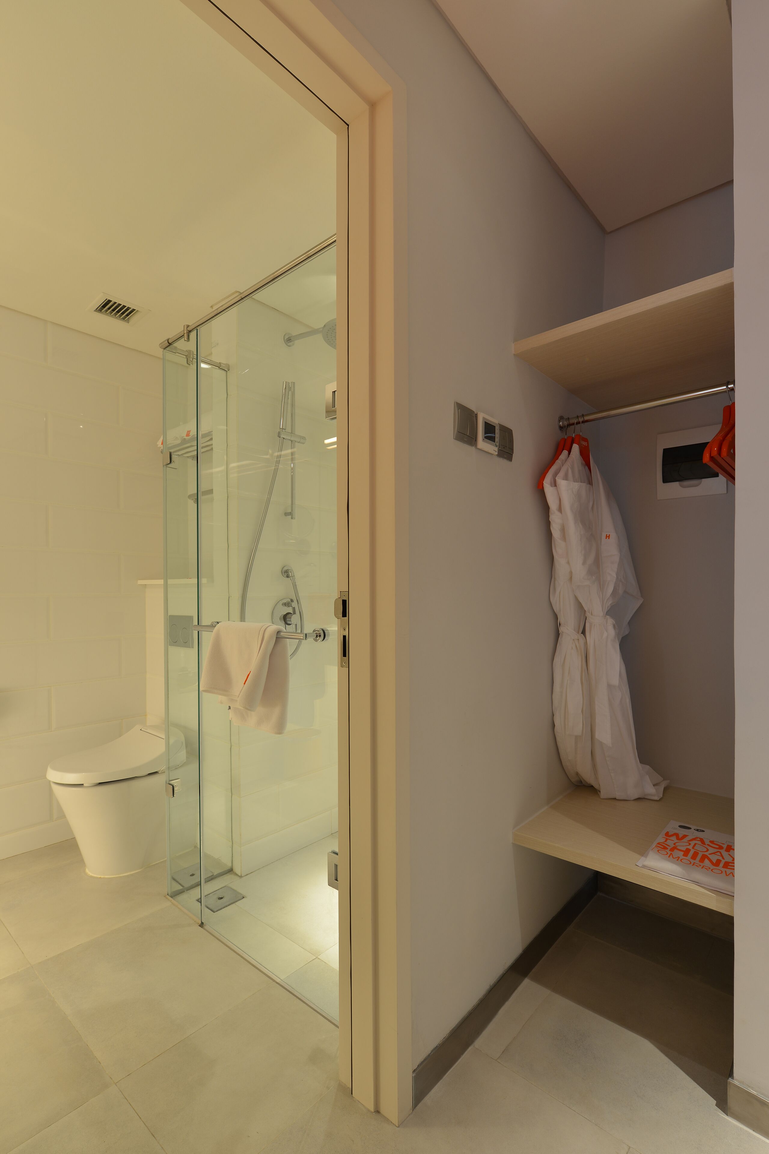 Un baño moderno con ducha de vidrio, inodoro y bata colgada en un perchero.
