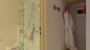 Un baño moderno con ducha de vidrio, inodoro y bata colgada en un perchero.