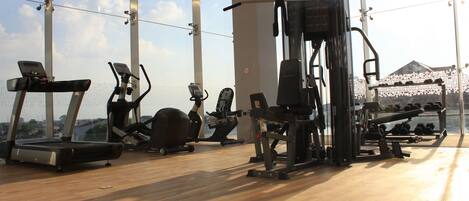Academia com máquinas de cardio, equipamentos de peso e uma grande janela com vista.