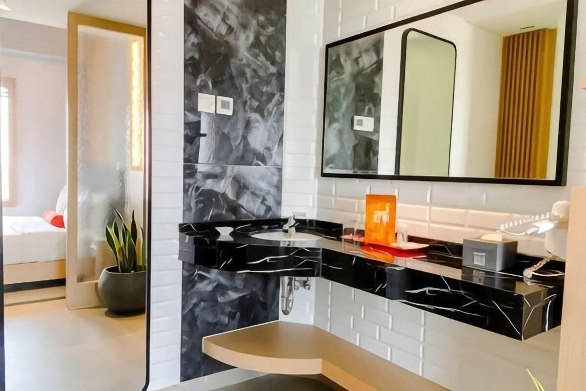 A modern bathroom with a black marble sink, a mirror, and a potted plant.