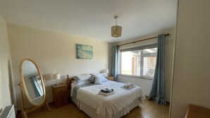 Una camera da letto con un letto, un comodino, uno specchio, una finestra con tende e un quadro appeso al muro.