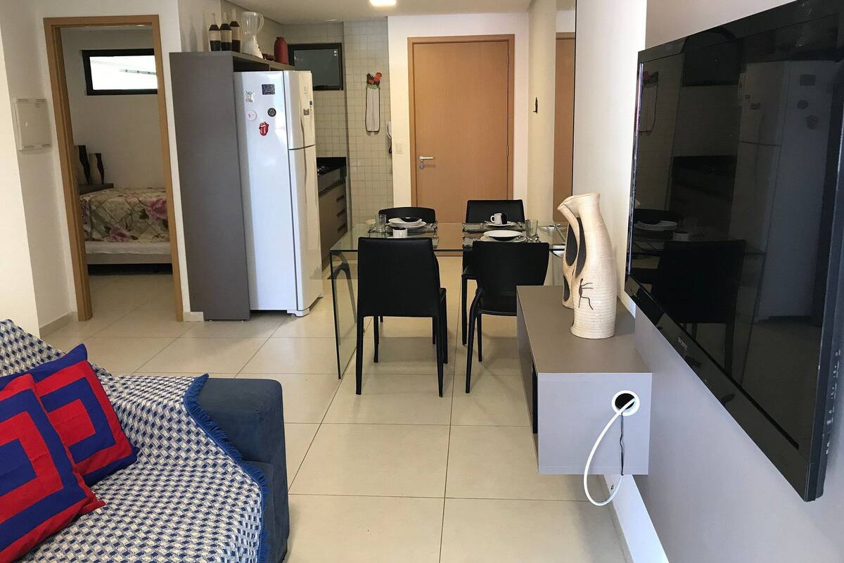 Un espacio habitable compacto con kitchenette, comedor, sofá con cojines estampados y televisor de pantalla plana.