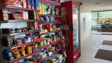 Una máquina expendedora de bebidas con el logotipo de Coca-Cola, estantes llenos de diversas botanas y bebidas, y un cartel arriba que indica una compra rápida.