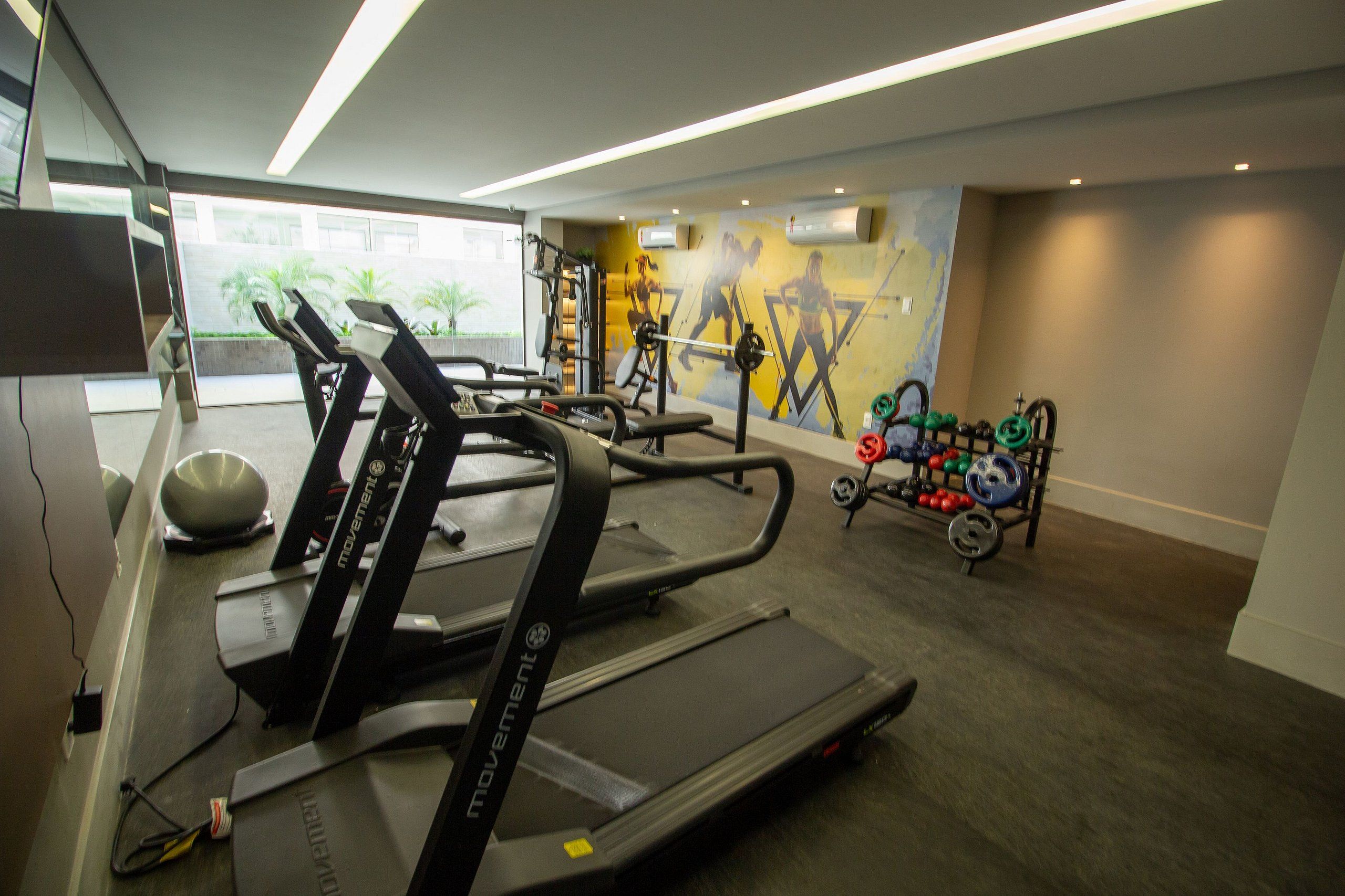 Ett gym med löpband, styrketräningsutrustning och en väggmålning.
