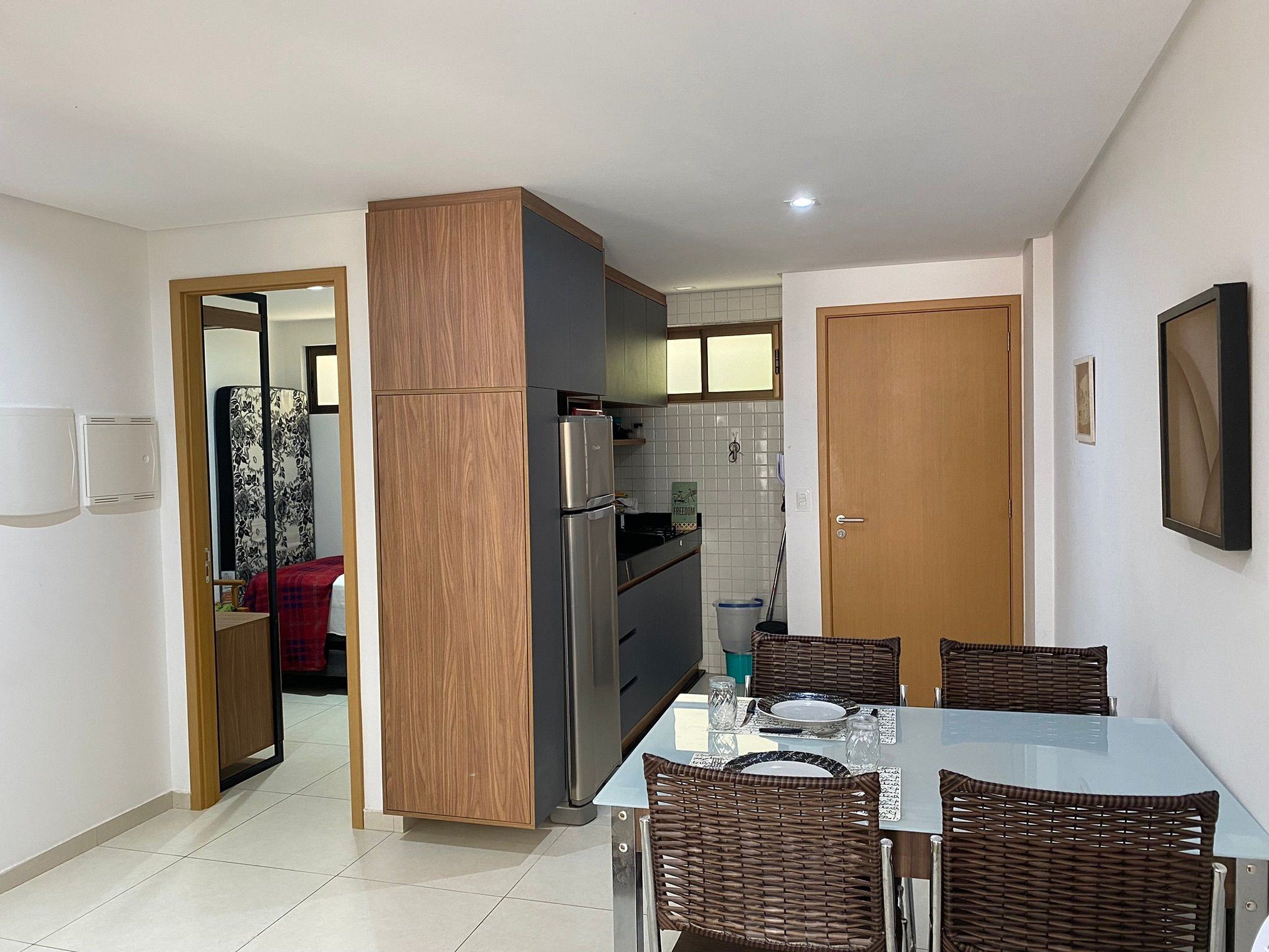 A compact kitchen with a refrigerator, a dining table with chairs, and a small window.
