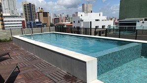 Une piscine sur le toit offrant une vue sur le paysage urbain, une terrasse en bois et un bâtiment moderne en arrière-plan.