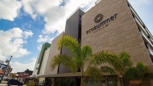 Un bâtiment moderne dont la façade porte l’inscription « ecosummer », entouré de palmiers.