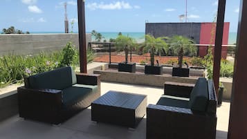 Un espacio con mesas al aire libre que ofrece vistas al océano y un edificio al fondo.