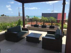 Uma área de estar ao ar livre com vista para o oceano e um edifício ao fundo.