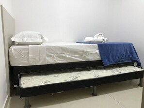Ein Einzelbett mit weißer Matratze, einer blauen Decke und einem aufgerollten weißen Handtuch.