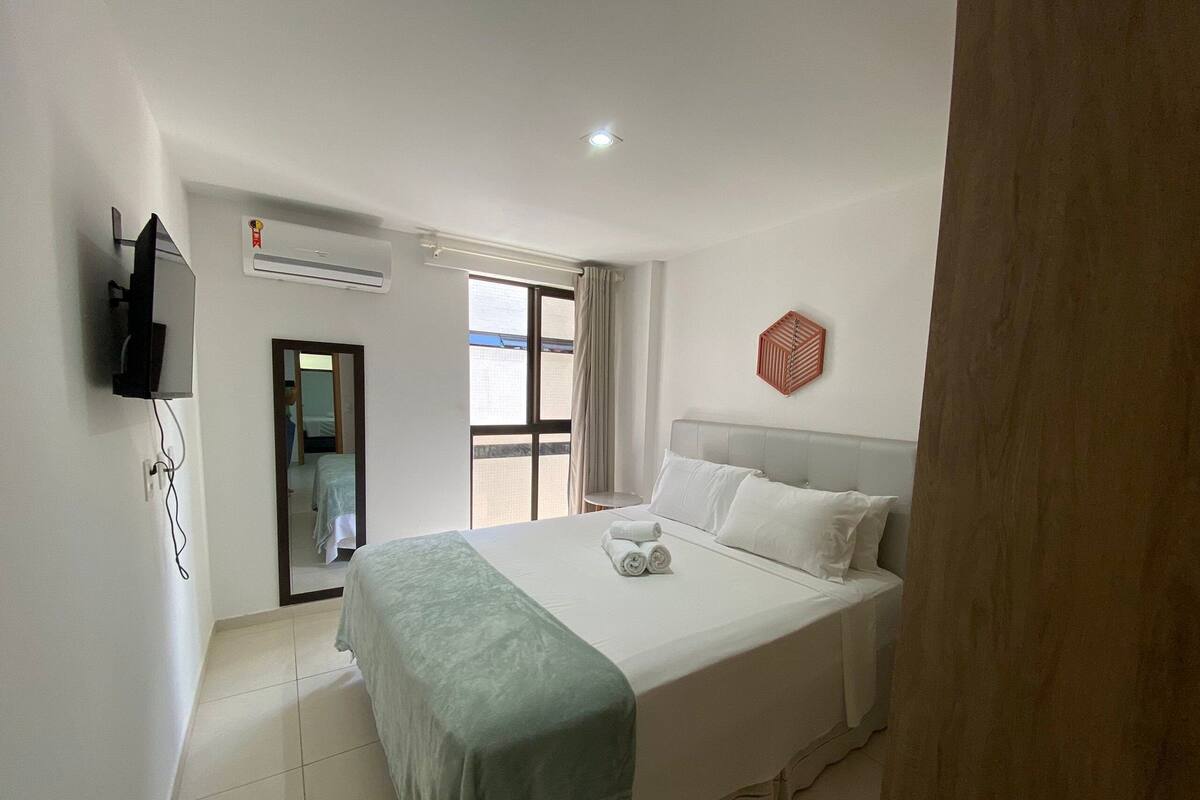 Habitación de hotel con una cama, televisión montada en la pared, aire acondicionado y una ventana con cortinas.