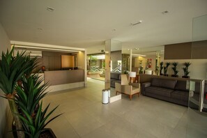 A modern lobby with a reception desk, seating area, and potted plants. - Bela Hospedagem - EcoSummer Flats Tambaú (João Pessoa)
