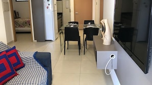 A compact living space with a kitchenette, a dining area, a sofa with patterned cushions, and a flat-screen TV. - Bela Hospedagem - EcoSummer Flats Tambaú (João Pessoa)