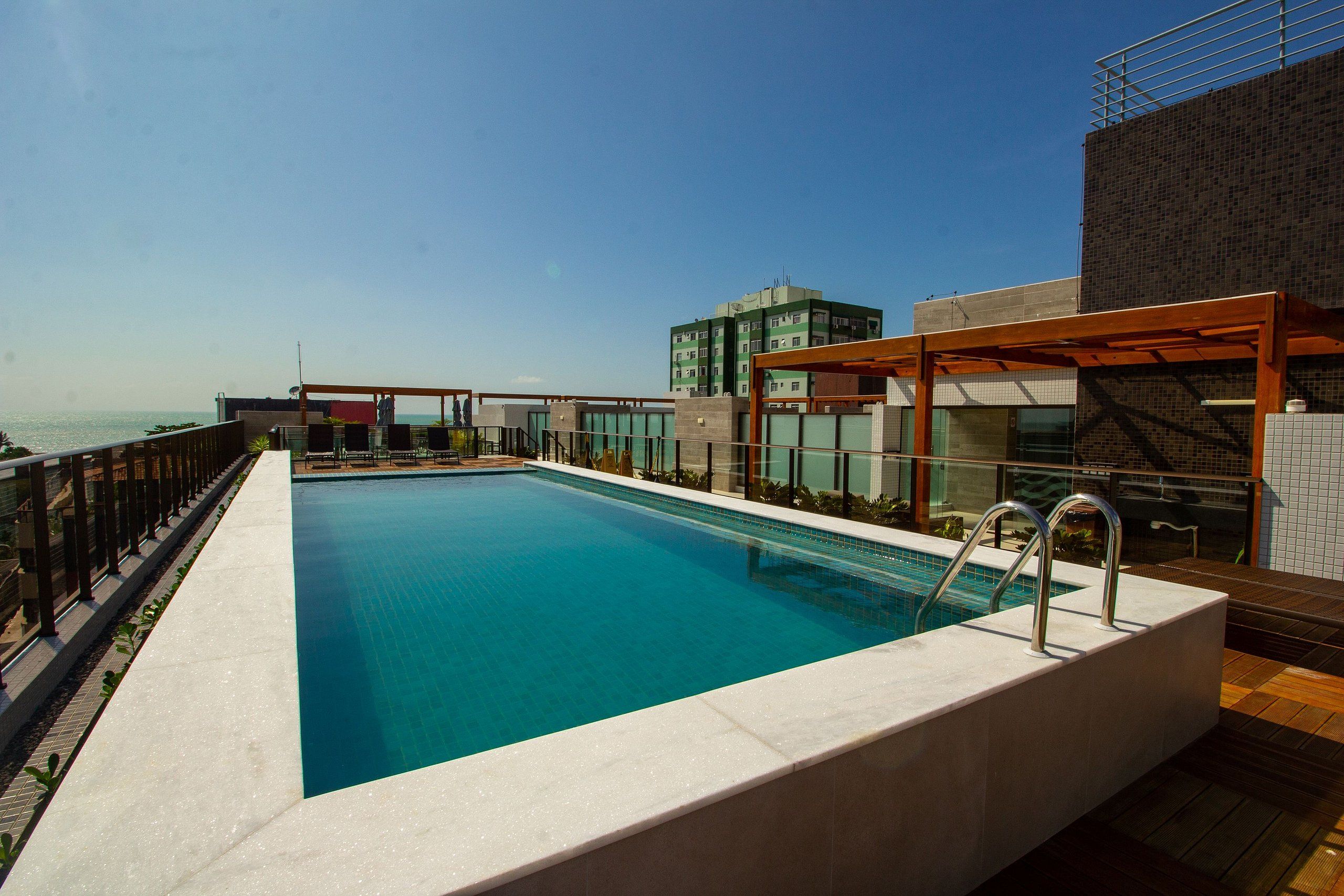 A rooftop swimming pool with a view of the sea, surrounded by modern buildings.