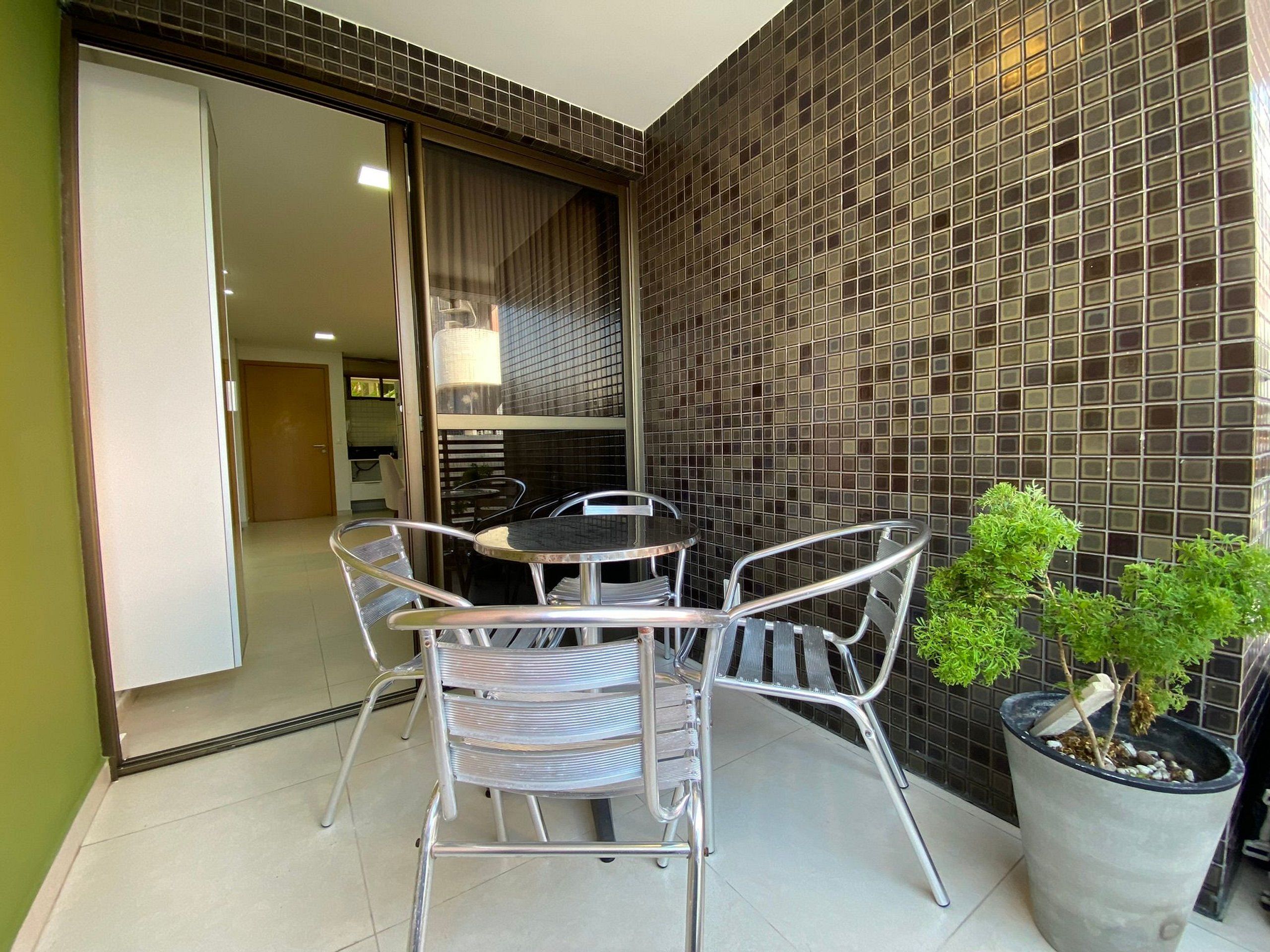 Uma área de pátio com mesa e cadeiras, um vaso de planta e uma parede revestida de azulejos.