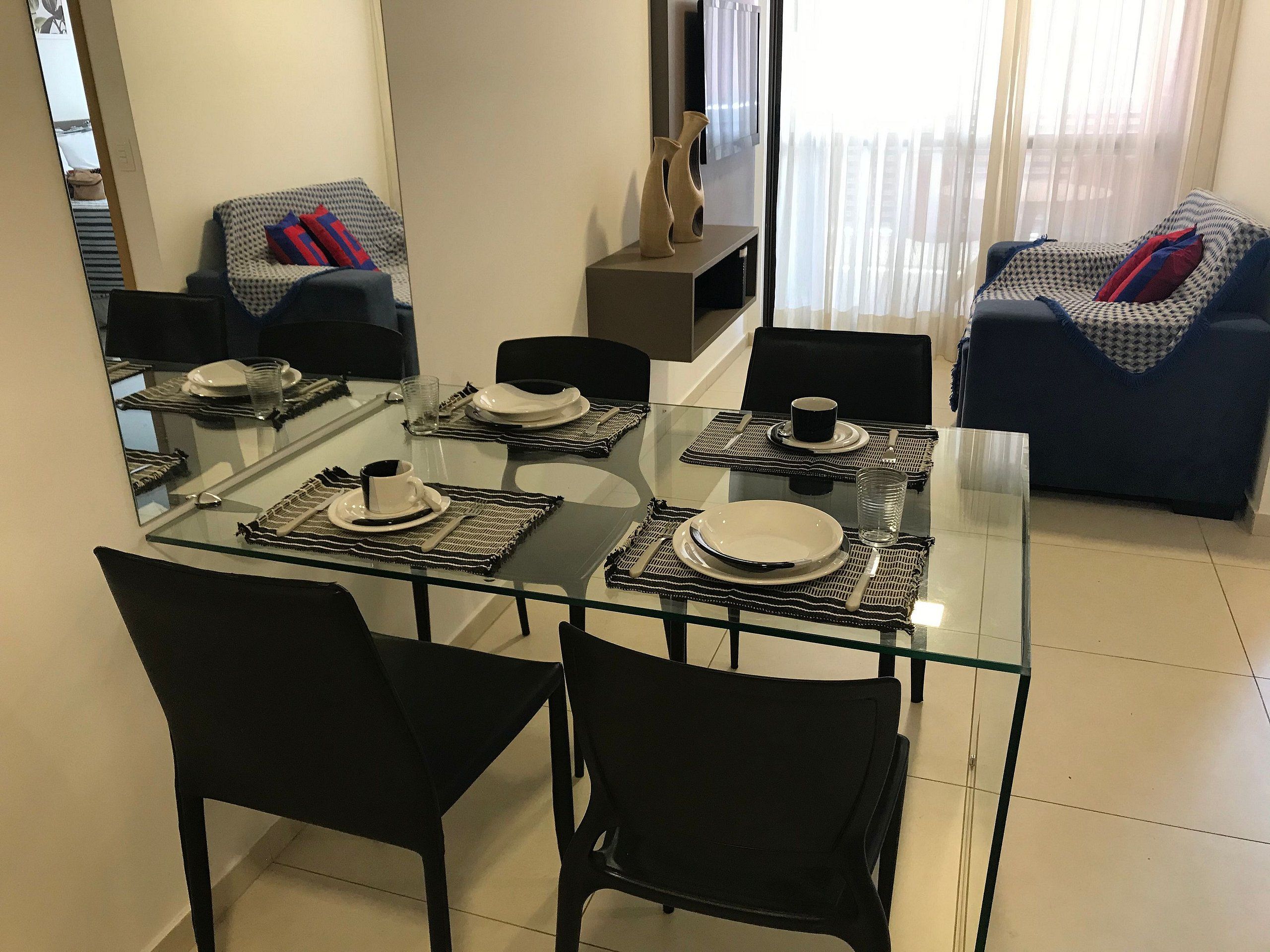 A dining area with a glass table, black chairs, and a sofa with patterned cushions.
