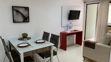 Un comedor con una mesa lista para dos personas, una mesita auxiliar roja, un televisor montado en la pared y un sofá.