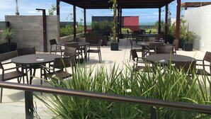 An outdoor patio with tables and chairs, a pergola, and potted plants. - Bela Hospedagem - EcoSummer Flats Tambaú (João Pessoa)