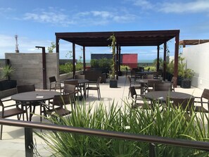 An outdoor patio with tables and chairs, a pergola, and potted plants. - Bela Hospedagem - EcoSummer Flats Tambaú (João Pessoa)