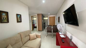 Una sala de estar con sofá, televisión, ventilador y un escritorio rojo con control remoto.