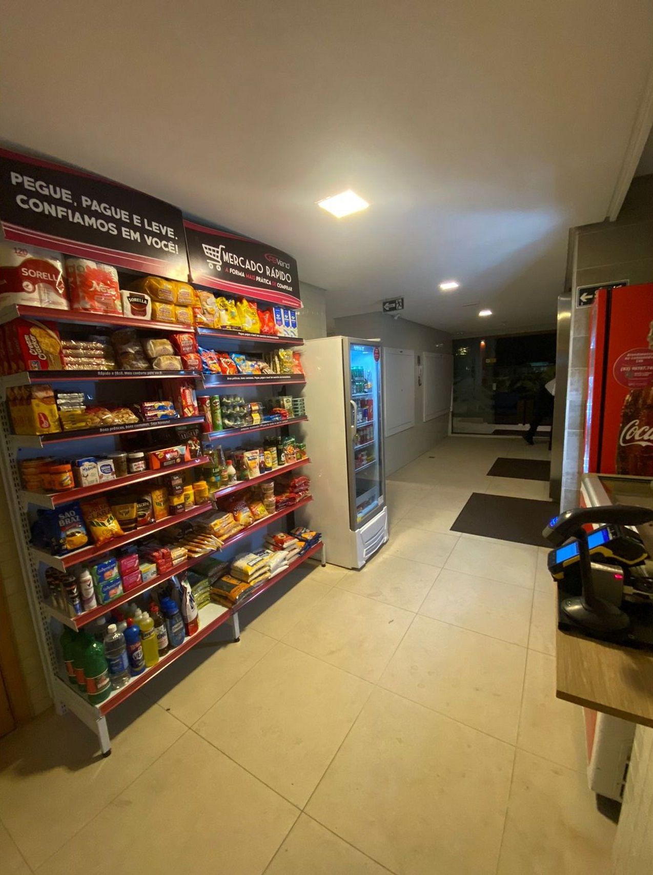 Un pasillo con estantes llenos de aperitivos y bebidas, una máquina expendedora y un refrigerador de Coca-Cola.