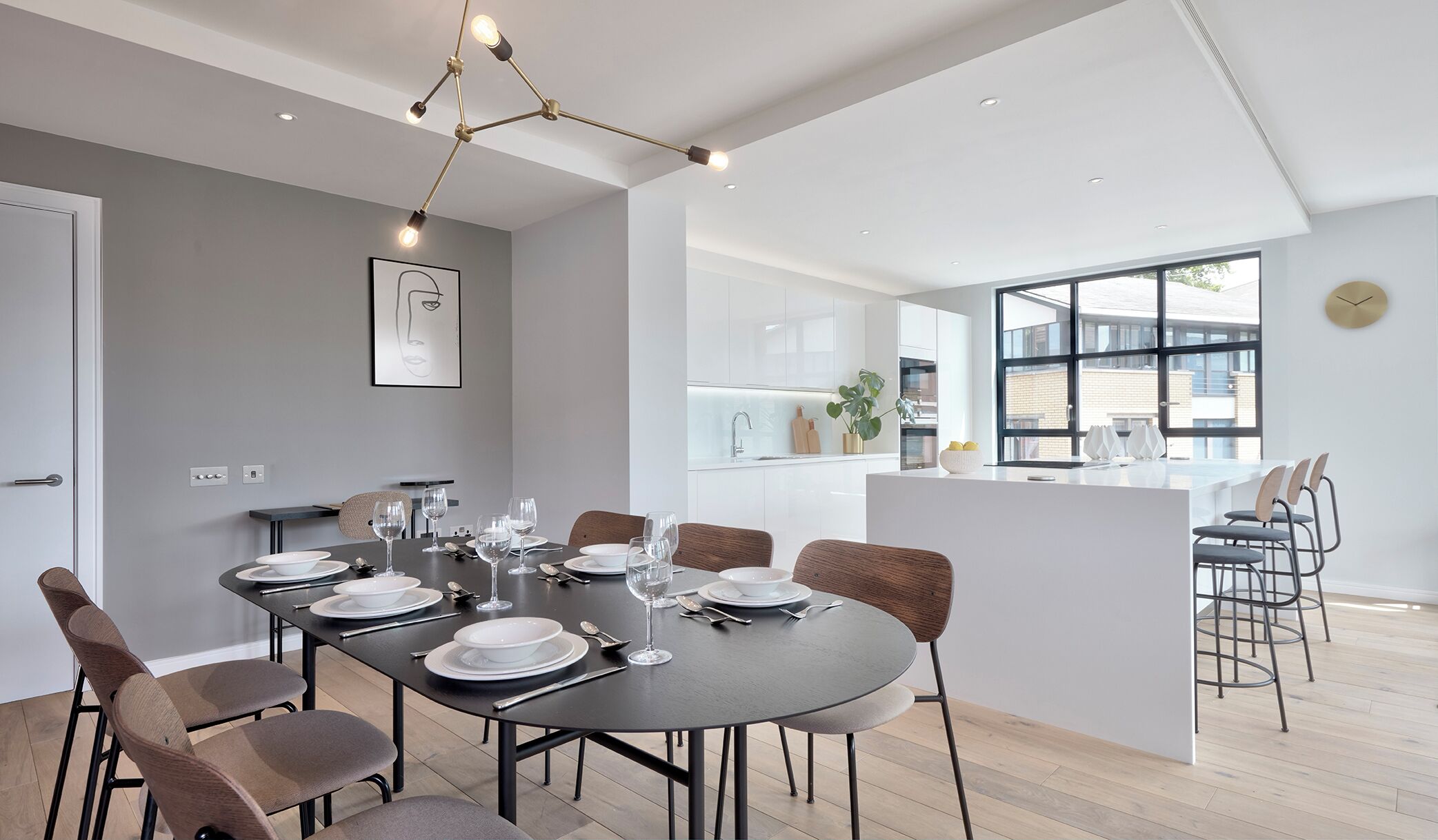 A modern dining area with a round table set for six, a kitchen with a large window, and a minimalist design.