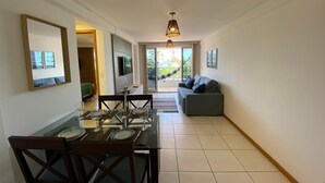 Un área de comedor con una mesa preparada para cuatro personas, un sofá, un televisor montado en la pared y vistas al exterior.