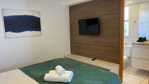 A hotel room with a bed, a TV mounted on a wooden panel, and a bathroom visible through an open door. - Bela Hospedagem - Atl Sul em Cabo Branco (João Pessoa)