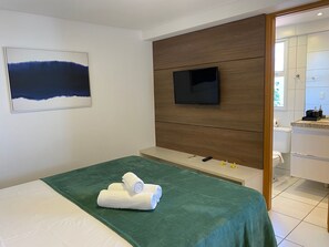 Habitación de hotel con cama, televisor montado en un panel de madera y baño visible a través de una puerta abierta.