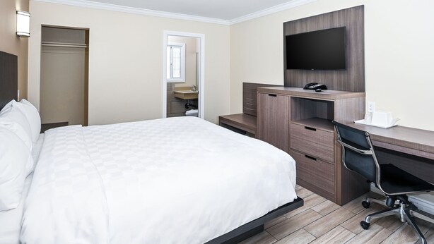 Une chambre d’hôtel avec un lit, un bureau et une chaise, une télévision et une salle de bain visible à travers une porte ouverte.